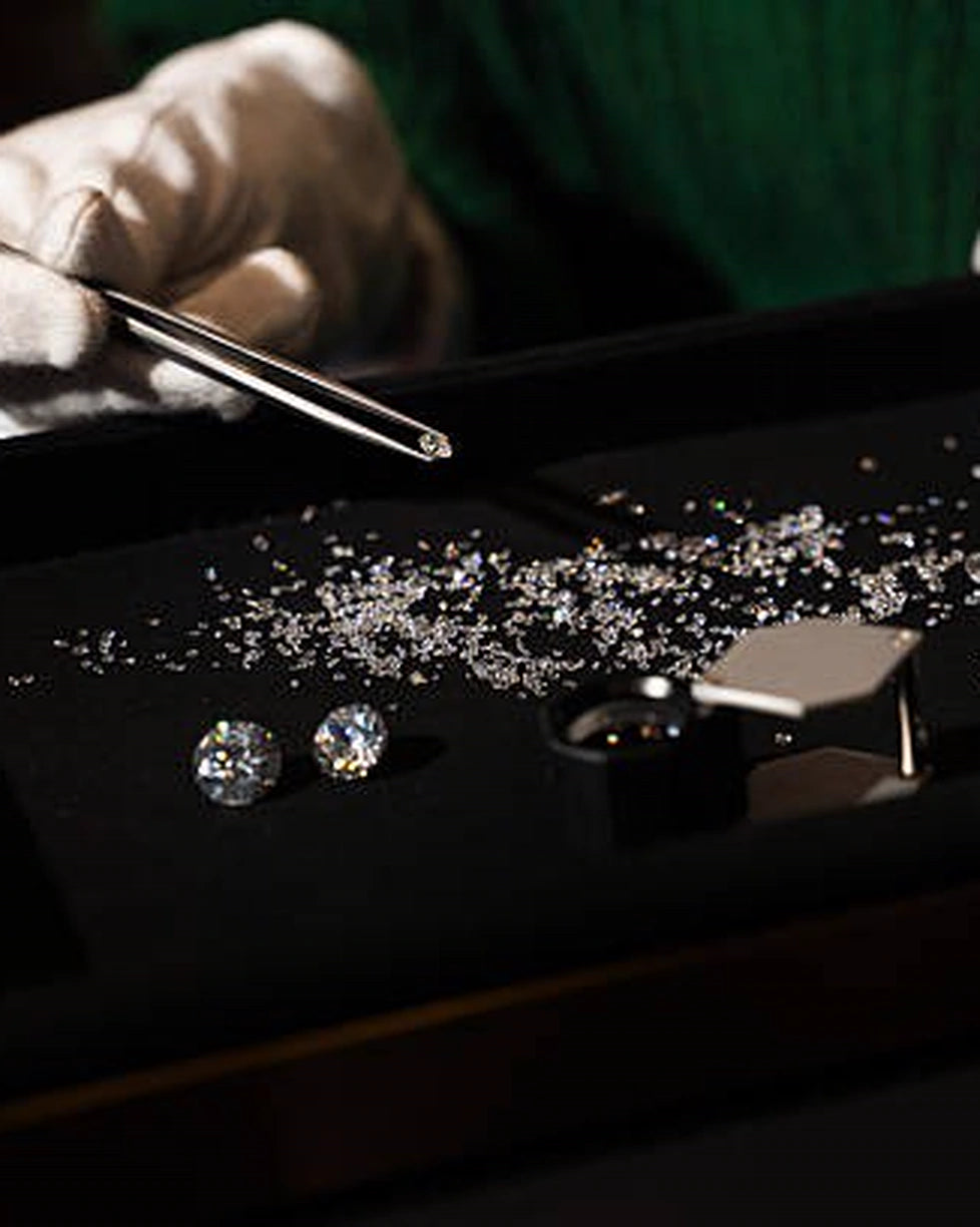 Gloved hands selecting loose stones with tweezers on a dark jewelry tray